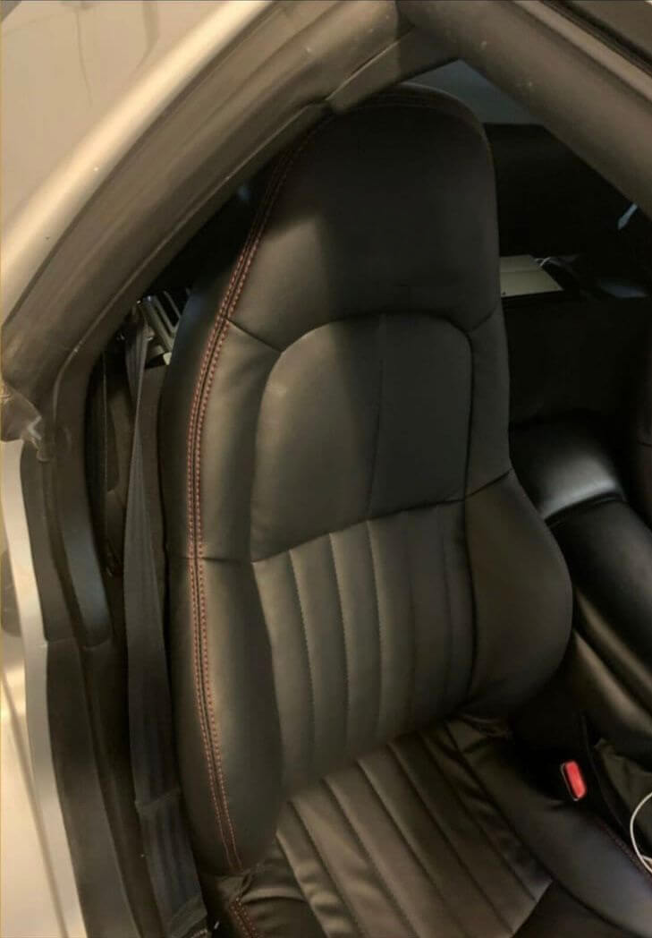 Installed black leather replacement car seat cover for a Corvette C5 with red stitching and an embroidered Corvette emblem on the headrest, shown inside a Corvette vehicle.